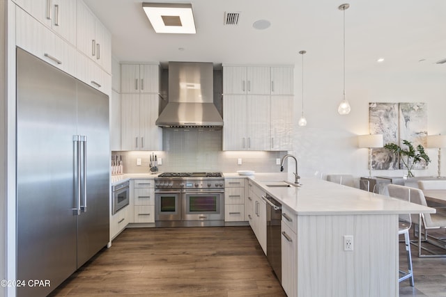 kitchen featuring a kitchen bar, decorative backsplash, premium appliances, wall chimney range hood, and hanging light fixtures