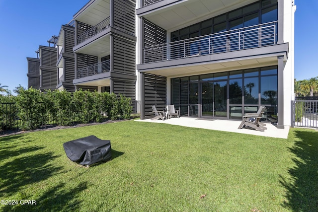 rear view of house featuring a lawn, a balcony, and a patio