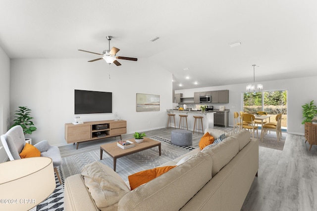 living room featuring ceiling fan with notable chandelier, lofted ceiling, and light wood-type flooring