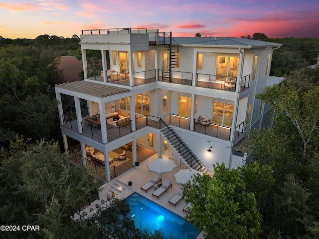 back house at dusk with a patio area, a balcony, and an outdoor hangout area