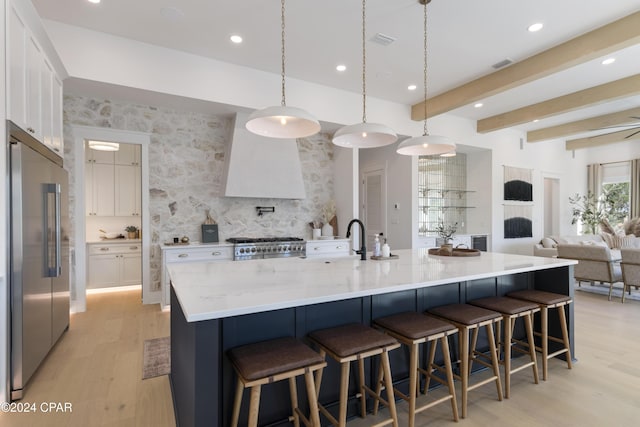 kitchen with appliances with stainless steel finishes, white cabinetry, a large island with sink, and pendant lighting