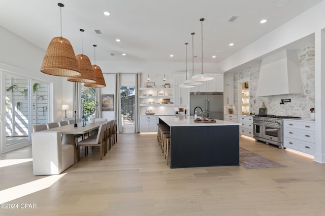 kitchen featuring wall chimney range hood, a spacious island, decorative light fixtures, white cabinets, and high end appliances