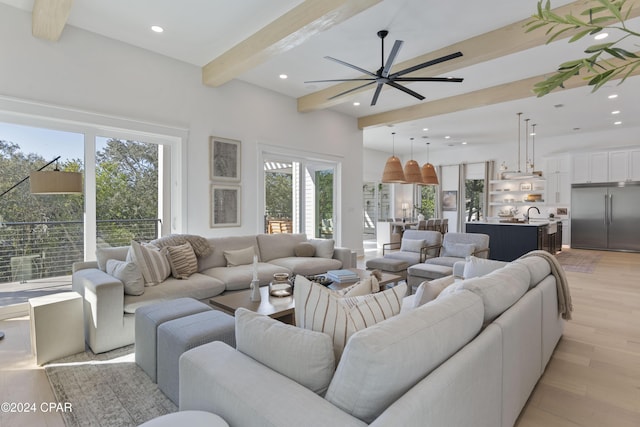 living room with beamed ceiling, ceiling fan, light wood-type flooring, and a wealth of natural light