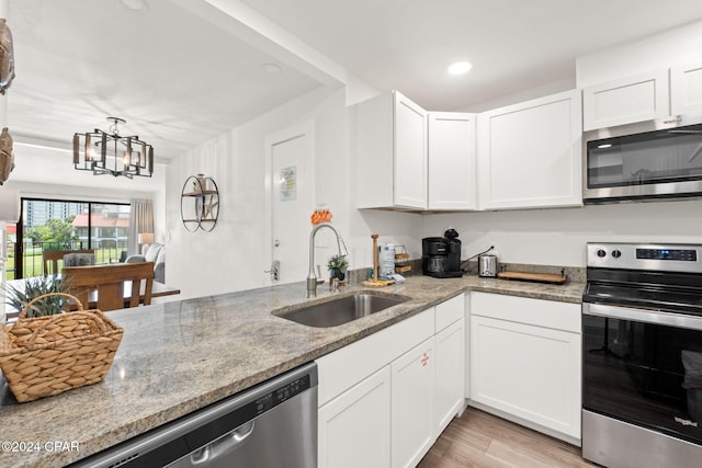 kitchen with light stone counters, stainless steel appliances, sink, a notable chandelier, and white cabinetry