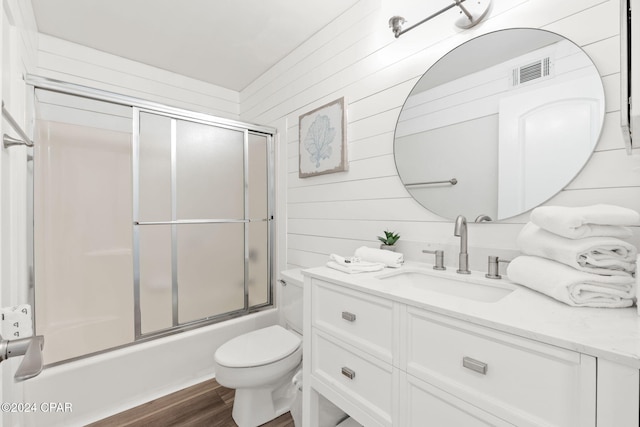 full bathroom featuring wood walls, bath / shower combo with glass door, wood-type flooring, toilet, and vanity