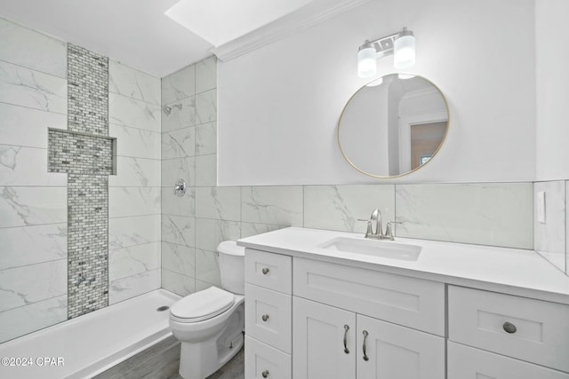 bathroom with toilet, tiled shower, tile walls, crown molding, and vanity