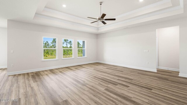 unfurnished living room featuring a raised ceiling, ceiling fan, light hardwood / wood-style flooring, and crown molding