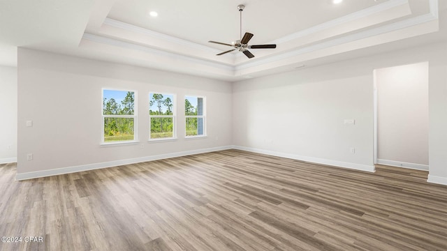 empty room with a tray ceiling, ceiling fan, crown molding, and light wood-type flooring