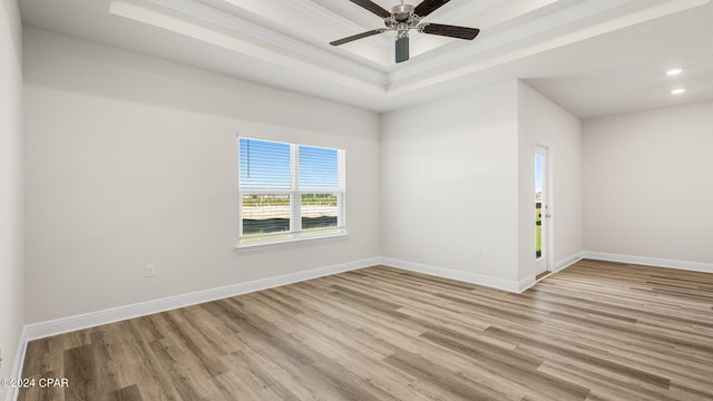 spare room featuring a tray ceiling, ceiling fan, and light wood-type flooring