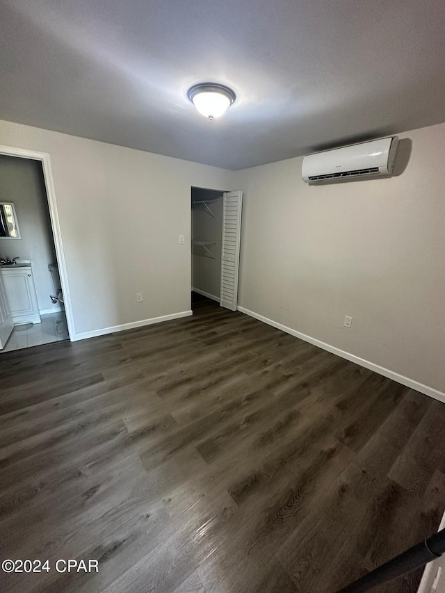 unfurnished bedroom featuring ensuite bathroom, an AC wall unit, and dark wood-type flooring