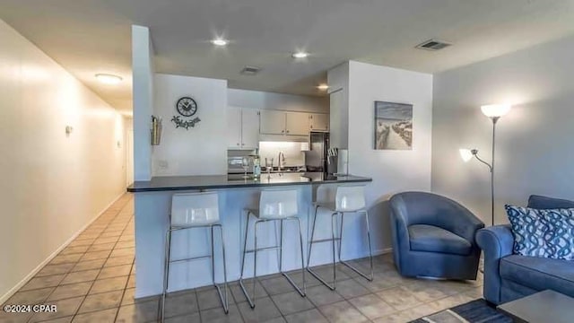 kitchen with kitchen peninsula, refrigerator, sink, white cabinets, and light tile patterned flooring