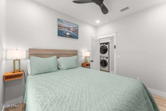 bedroom with ceiling fan, stacked washer / dryer, wood finished floors, visible vents, and baseboards