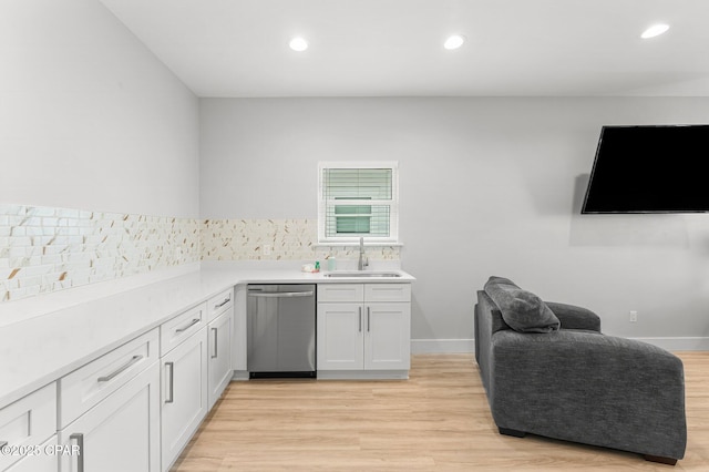 kitchen with light wood-style flooring, light countertops, stainless steel dishwasher, white cabinetry, and a sink