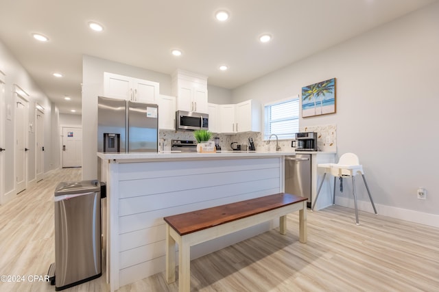 kitchen with decorative backsplash, appliances with stainless steel finishes, light wood-type flooring, sink, and white cabinetry