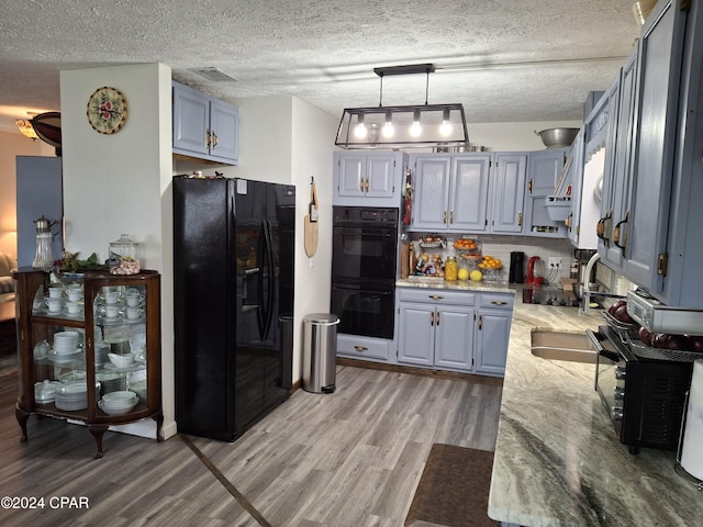 kitchen with pendant lighting, black appliances, a textured ceiling, light hardwood / wood-style floors, and light stone counters