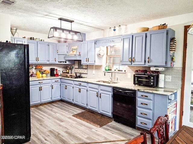 kitchen featuring light wood finished floors, light countertops, hanging light fixtures, a sink, and black appliances