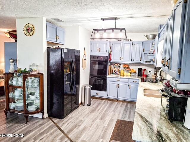 kitchen featuring black appliances, hanging light fixtures, a sink, and light wood-style floors