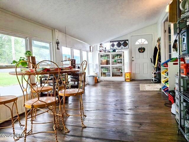 dining area with dark wood-style floors, vaulted ceiling, and a textured ceiling