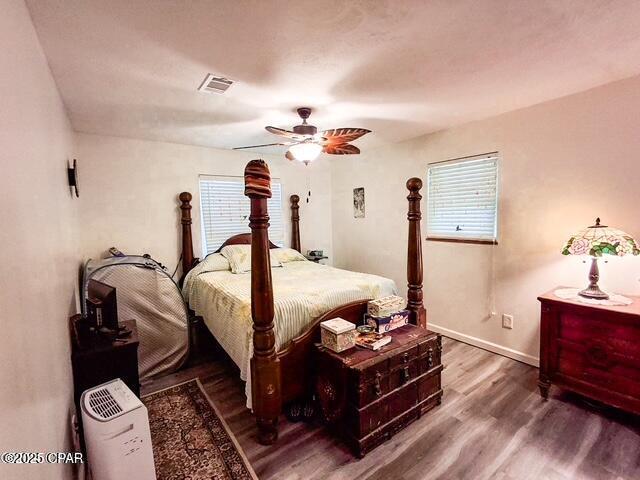 bedroom featuring baseboards, ceiling fan, visible vents, and wood finished floors