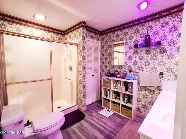 bathroom with wallpapered walls, toilet, wood finished floors, crown molding, and a closet