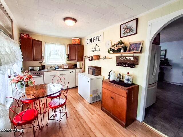 kitchen with light wood-style floors, arched walkways, freestanding refrigerator, and fridge