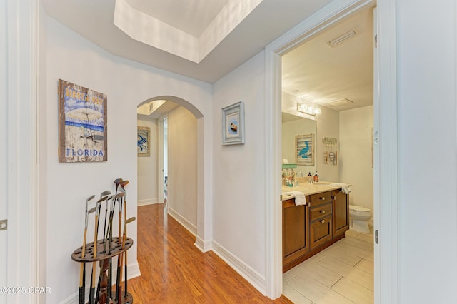 hall with visible vents, arched walkways, baseboards, light wood-style floors, and a sink