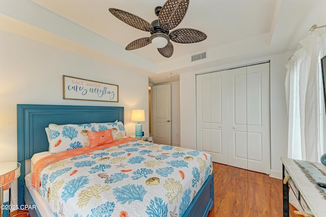 bedroom featuring light wood finished floors, visible vents, a raised ceiling, and a closet