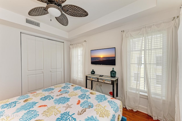 bedroom with ceiling fan, wood finished floors, visible vents, a closet, and a tray ceiling