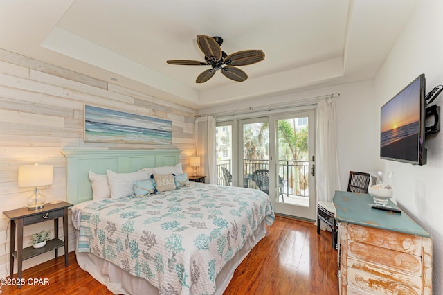 bedroom with access to exterior, a ceiling fan, a tray ceiling, and wood finished floors