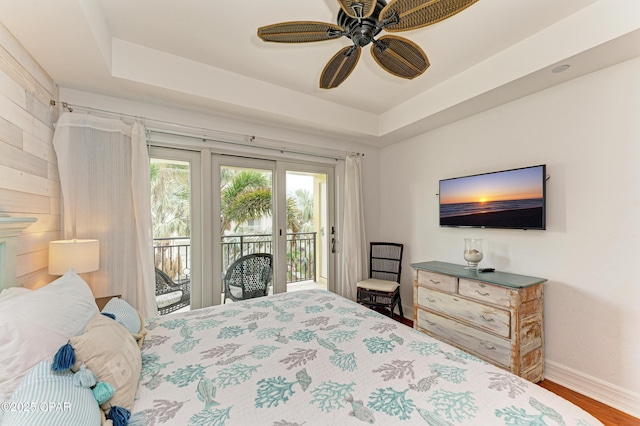 bedroom with wood finished floors, a ceiling fan, baseboards, access to outside, and a tray ceiling