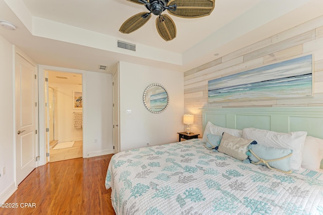 bedroom with ceiling fan, wooden walls, wood finished floors, visible vents, and a tray ceiling