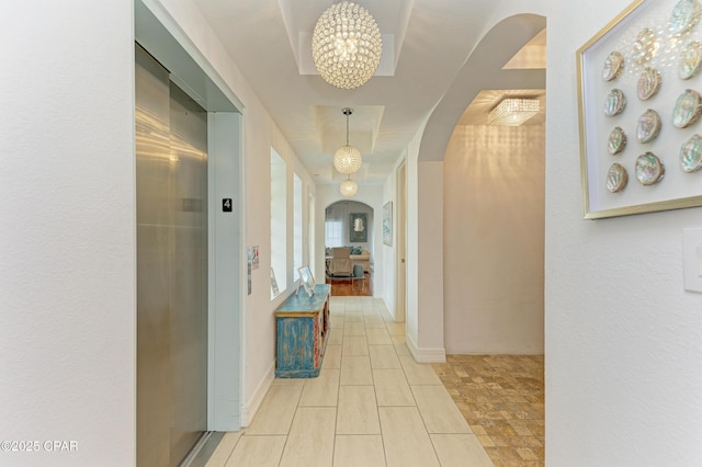 corridor with elevator, baseboards, arched walkways, and a notable chandelier