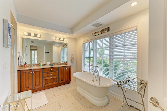 bathroom with a freestanding bath, double vanity, a sink, and visible vents