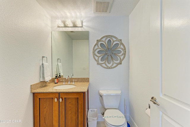 bathroom featuring baseboards, visible vents, a textured wall, toilet, and vanity