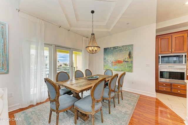 dining area with a chandelier, baseboards, a raised ceiling, and light wood-style floors