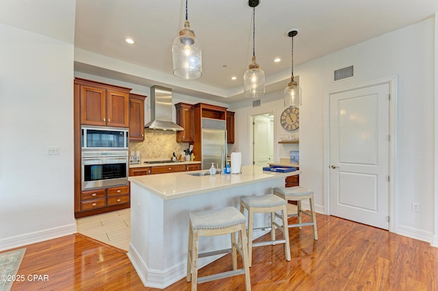 kitchen featuring visible vents, built in appliances, light countertops, light wood-type flooring, and wall chimney range hood