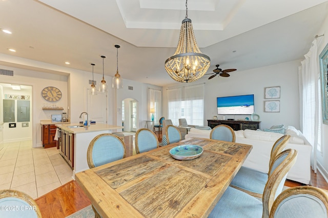 dining room with arched walkways, a tray ceiling, light wood-type flooring, and recessed lighting