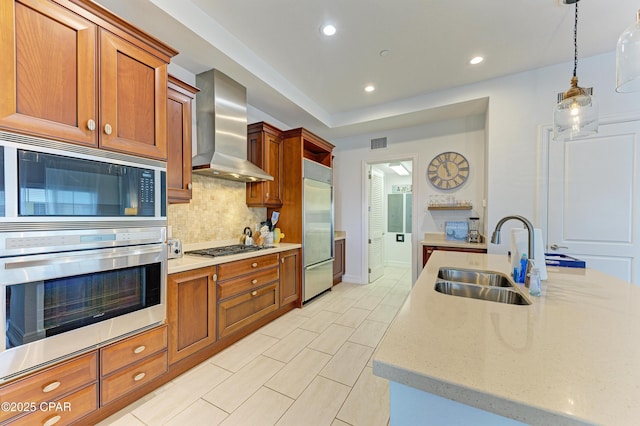 kitchen with built in appliances, a sink, visible vents, wall chimney range hood, and tasteful backsplash