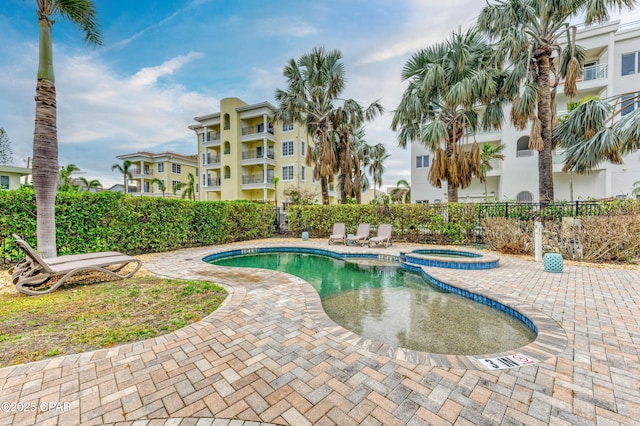 view of swimming pool featuring a pool with connected hot tub, fence, and a patio