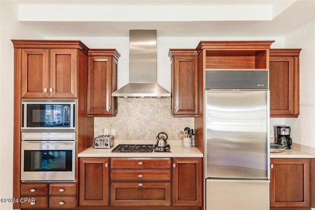 kitchen with built in appliances, wall chimney range hood, and tasteful backsplash