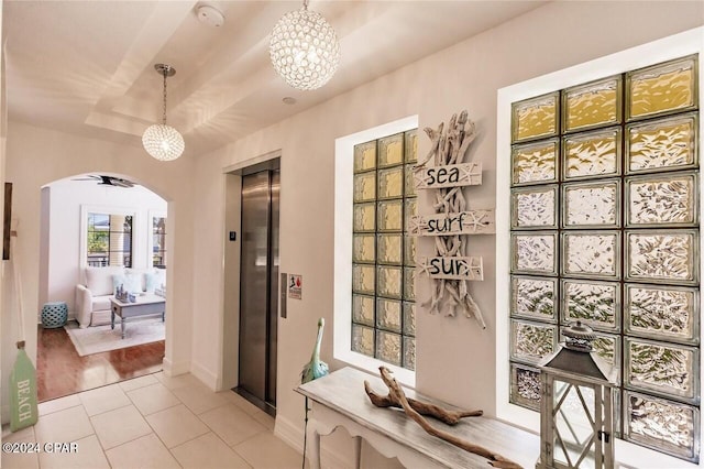 hall with a tray ceiling, elevator, light hardwood / wood-style floors, and a notable chandelier