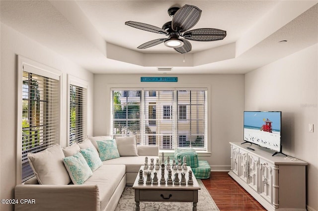 living room with a tray ceiling, a wealth of natural light, and dark hardwood / wood-style floors