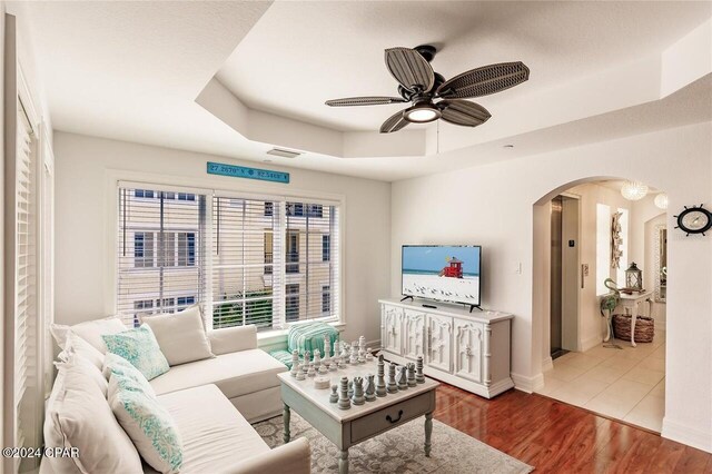 living room with a raised ceiling, ceiling fan, and hardwood / wood-style floors