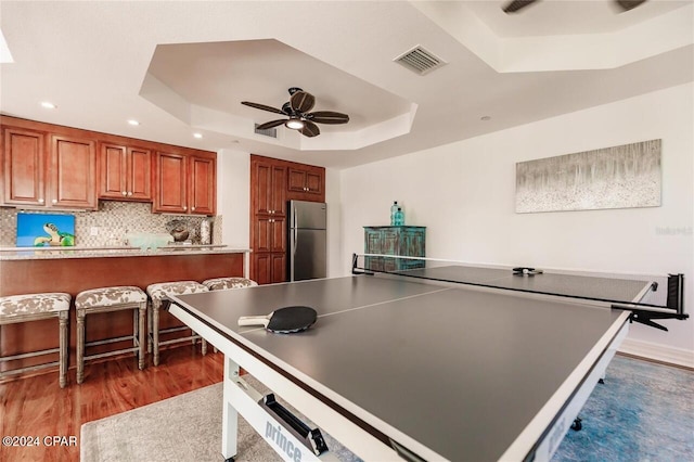 rec room with ceiling fan, a raised ceiling, and dark wood-type flooring