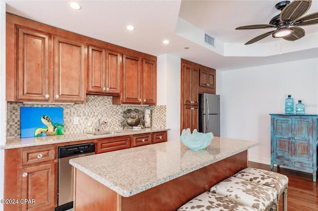 kitchen with a breakfast bar area, backsplash, appliances with stainless steel finishes, brown cabinetry, and a sink