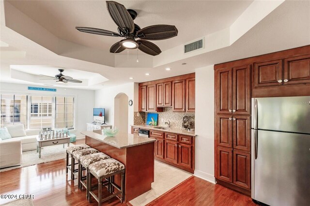 kitchen with stainless steel fridge, light stone counters, a raised ceiling, light hardwood / wood-style floors, and a breakfast bar area