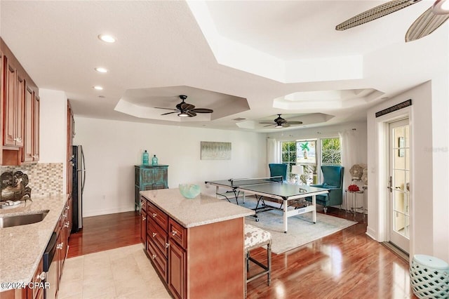 kitchen featuring light stone counters, a tray ceiling, a kitchen island, and light hardwood / wood-style flooring