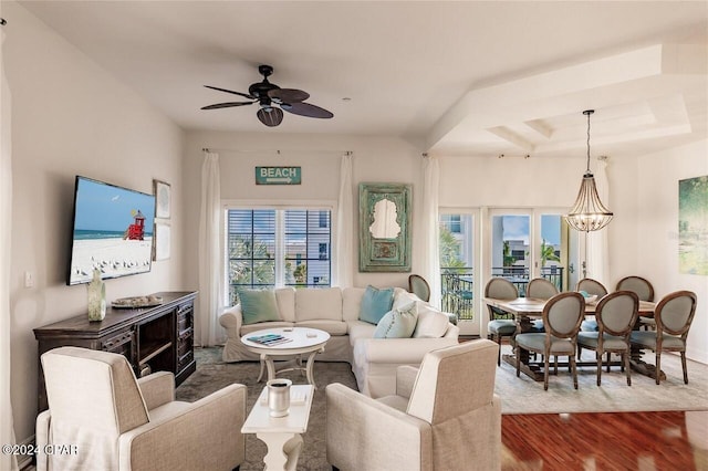 living room with wood-type flooring, ceiling fan with notable chandelier, and a raised ceiling