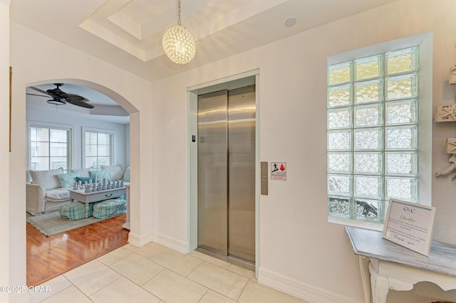 hall with light tile patterned floors, baseboards, arched walkways, elevator, and a tray ceiling