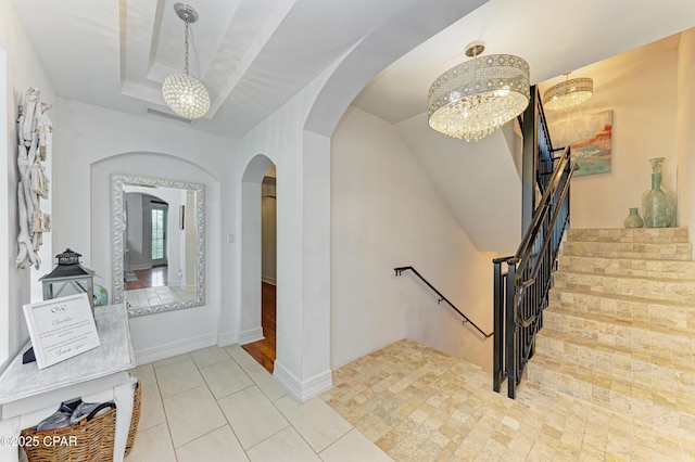 interior space with baseboards, visible vents, a raised ceiling, and arched walkways